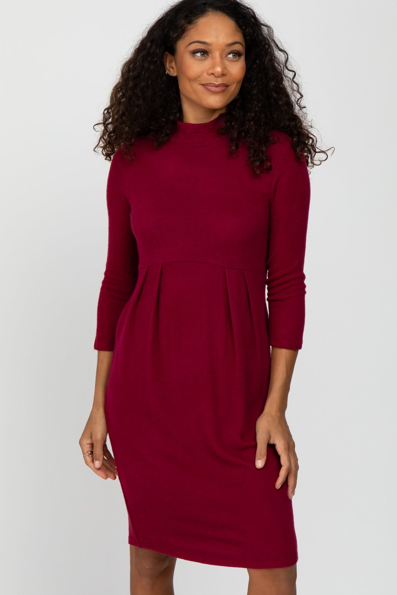 woman wearing a burgundy long sleeve dress with a fitted bodice and pleated skirt details