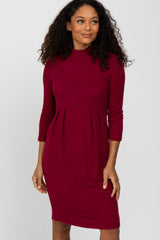 woman wearing a burgundy long sleeve dress with a fitted bodice and pleated skirt details
