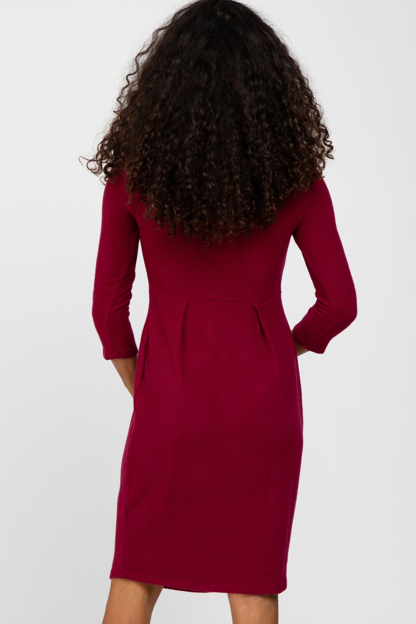 Back view of a woman with long curly hair wearing a burgundy three-quarter sleeve dress with pleated waist