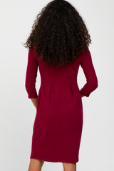Back view of a woman with long curly hair wearing a burgundy three-quarter sleeve dress with pleated waist