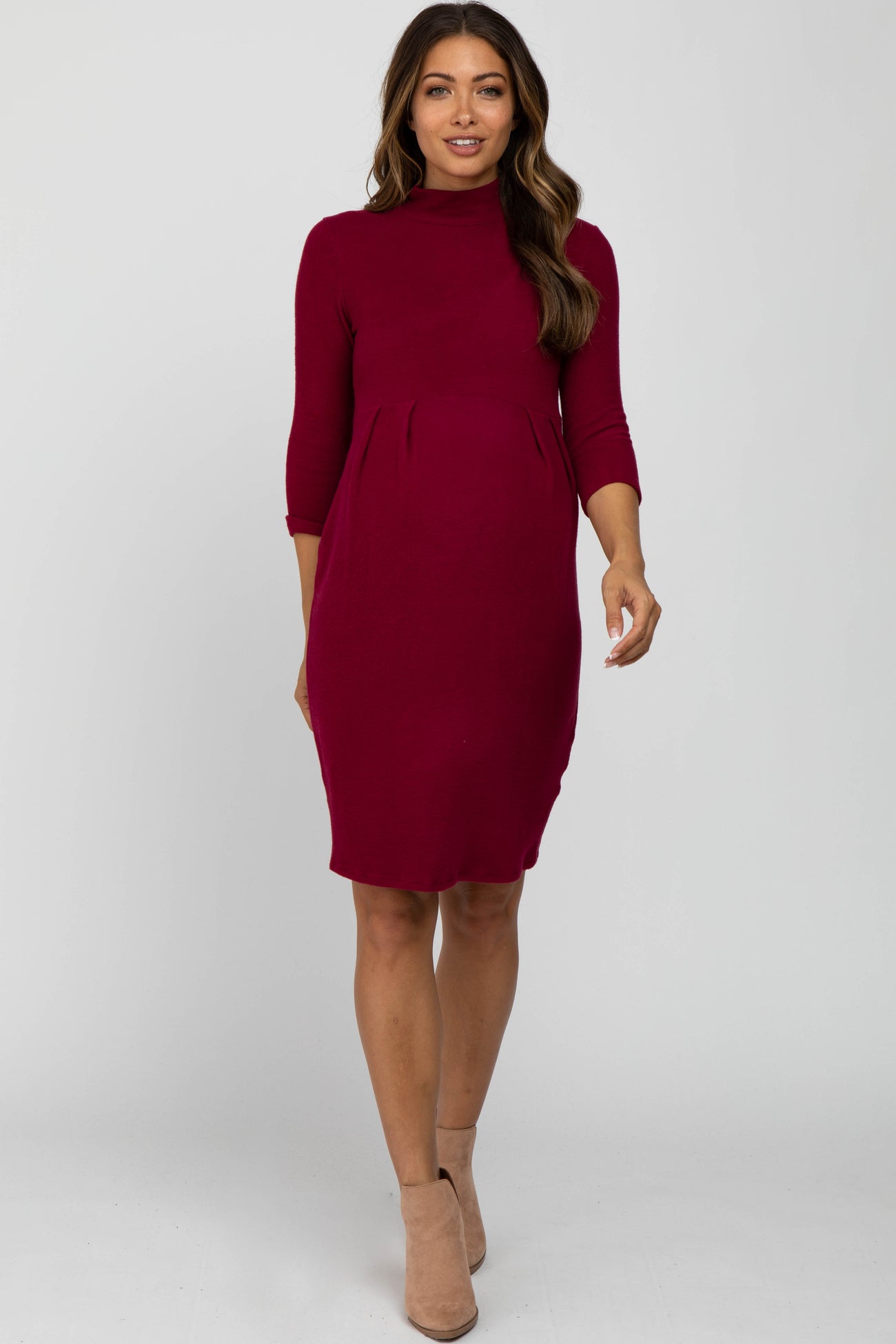 woman wearing a burgundy three-quarter sleeve maternity dress with a mock neck and tan ankle boots