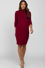 woman wearing a burgundy three-quarter sleeve maternity dress with a mock neck and tan ankle boots