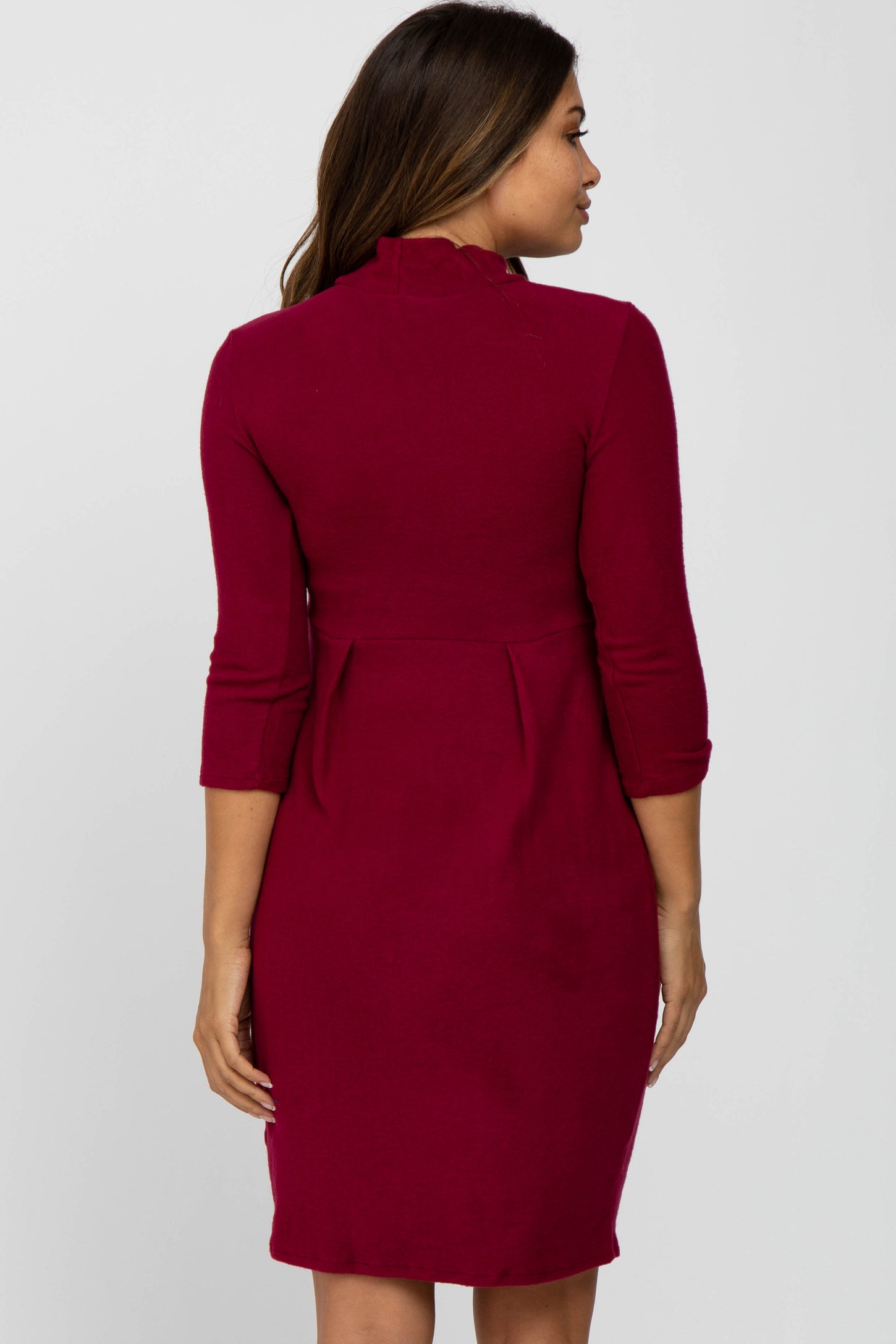 woman wearing a burgundy maternity dress with three-quarter sleeves and a pleated back design