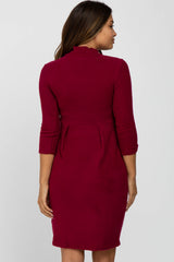 woman wearing a burgundy maternity dress with three-quarter sleeves and a pleated back design