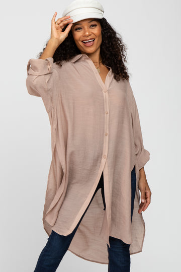 woman wearing a light pink oversized button-up shirt with rolled sleeves and smiling while adjusting her hat
