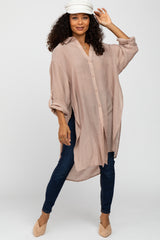 woman wearing a light pink oversized button-up shirt with rolled sleeves and dark skinny jeans, posing with a cap