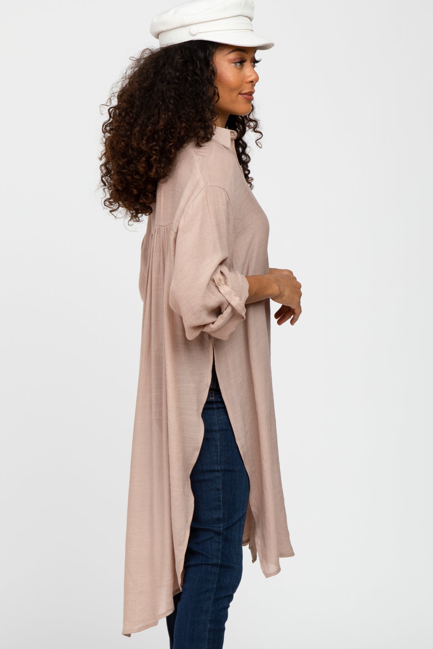 woman wearing a light pink long sleeve tunic with a high-low hem and rolled sleeves, styled with dark jeans and a white cap