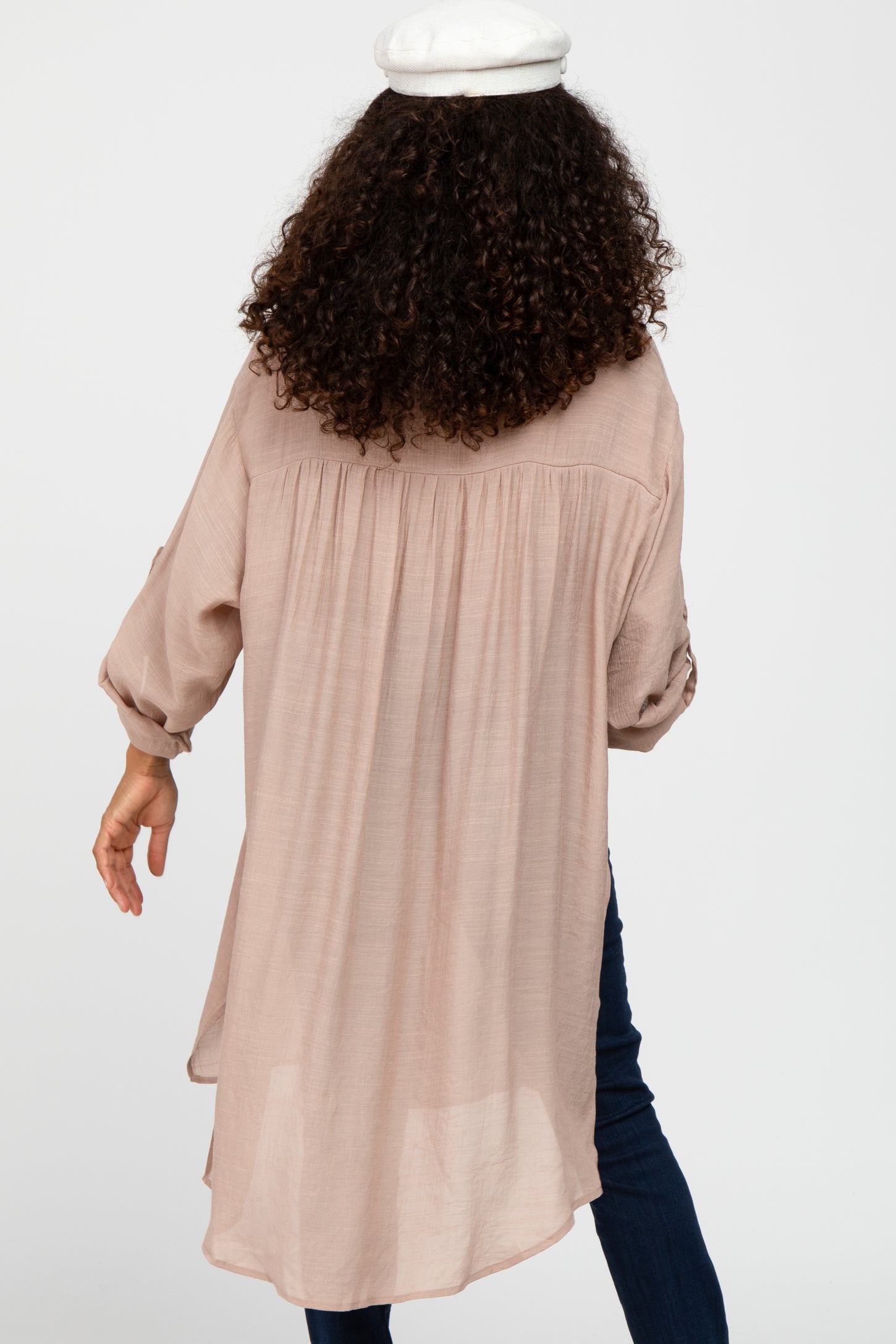 woman wearing a light pink long sleeve tunic with a curved hem and gathered back detail, seen from the back