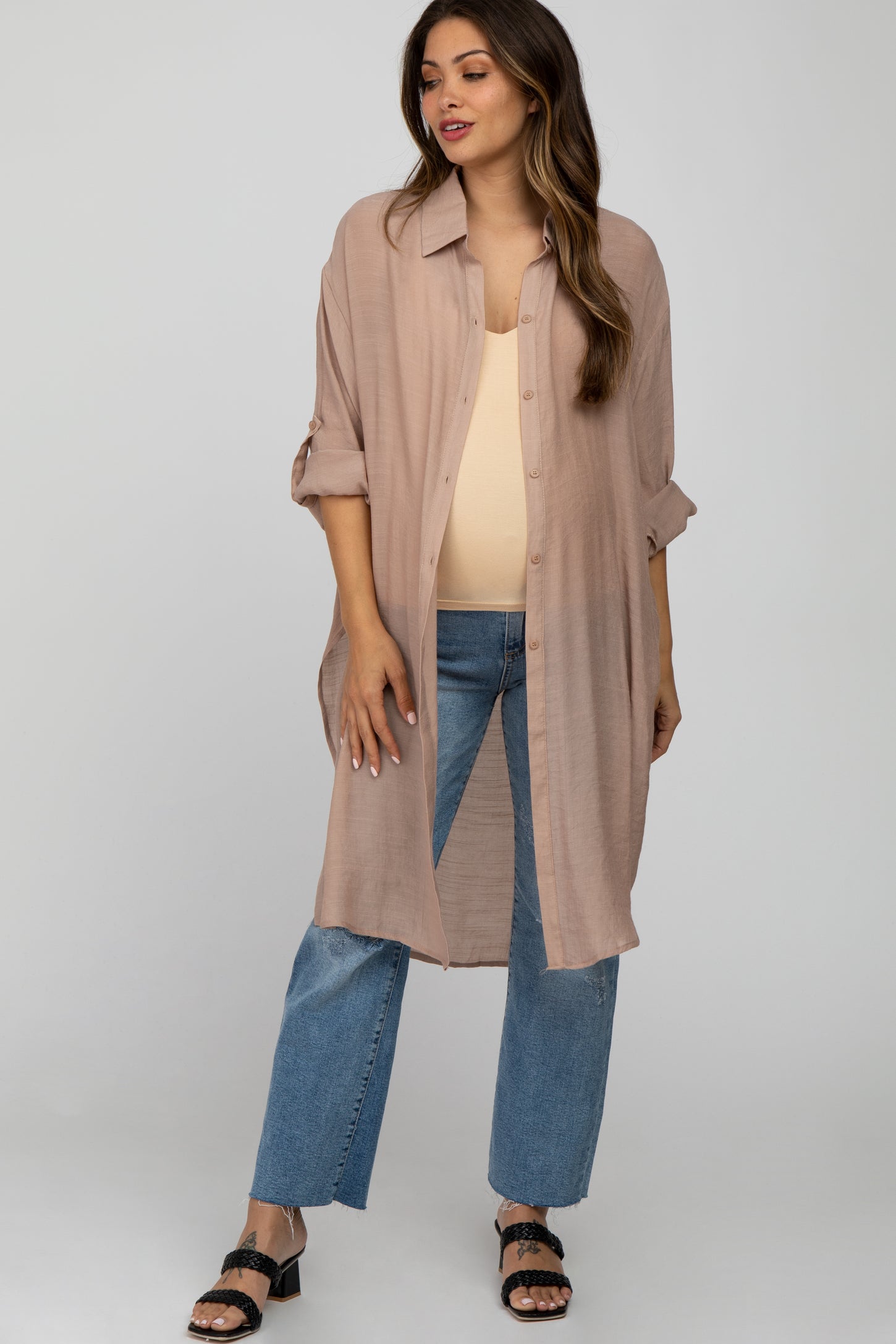 woman wearing a beige maternity shirt dress over a tank top, paired with light blue jeans, showcasing her baby bump