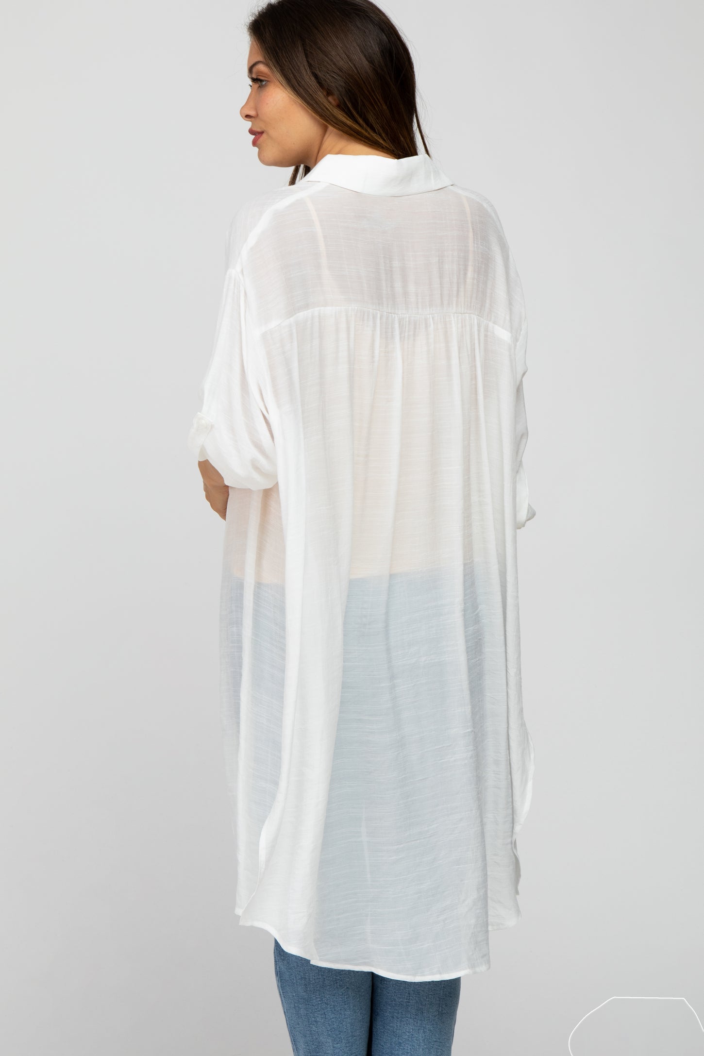 woman wearing a sheer white maternity tunic with a light blue gradient, shown from the back with loose fit and rolled sleeves