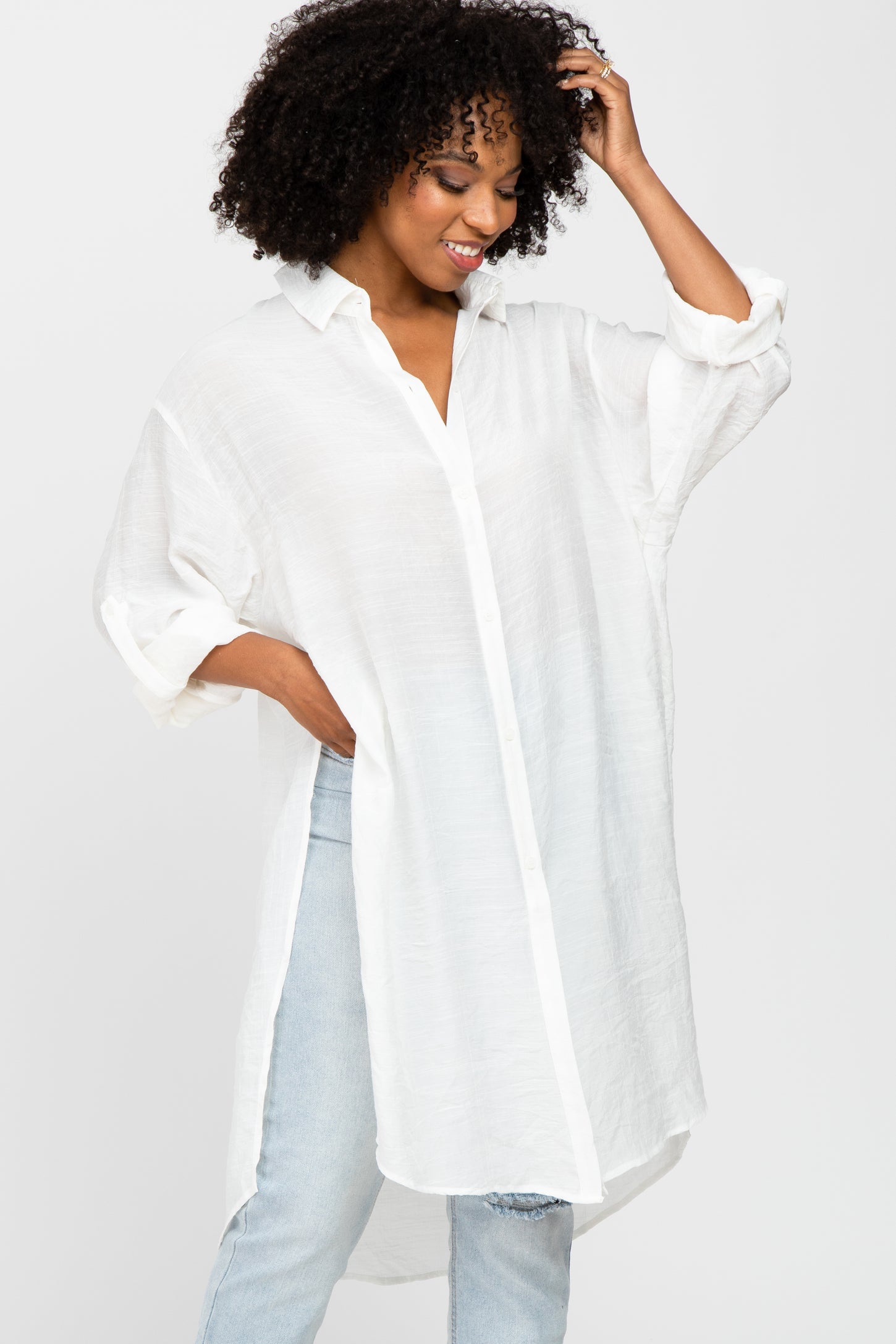 woman with curly hair wearing an oversized white button down tunic shirt and light wash jeans