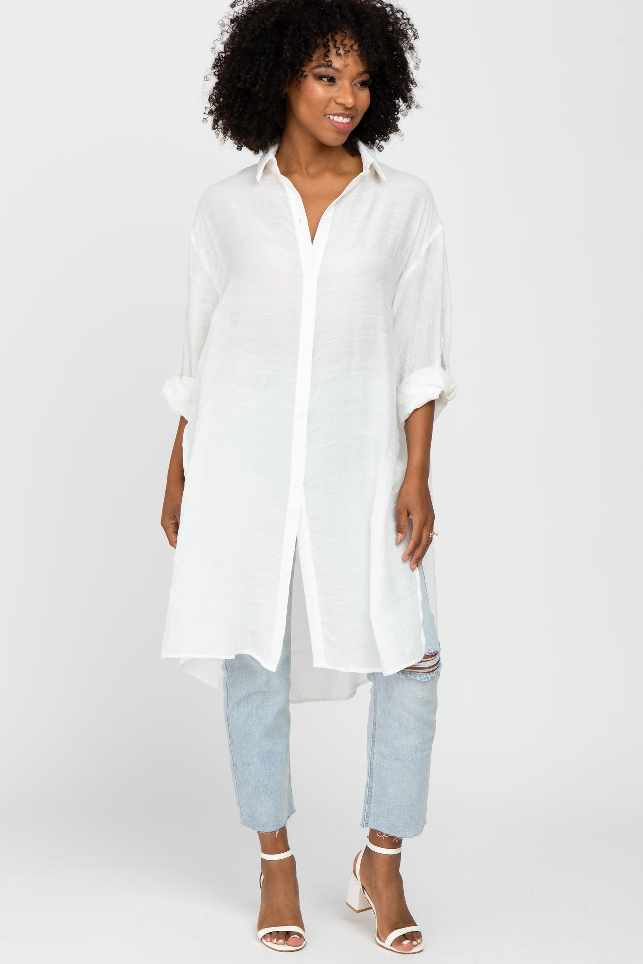 woman wearing a white long sleeve button-up tunic top with rolled sleeves and light blue distressed jeans
