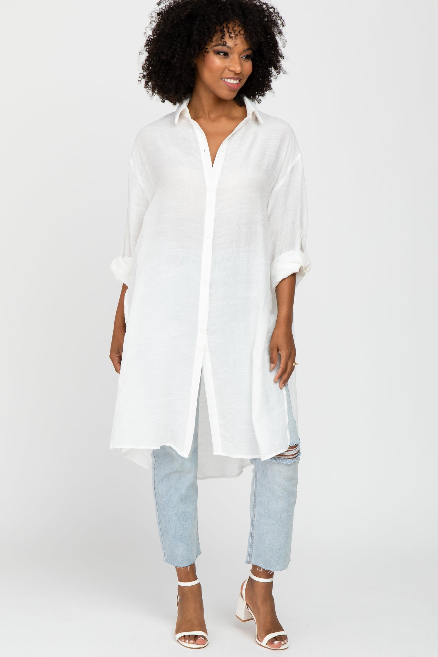 woman wearing a white long sleeve button-up tunic top with rolled sleeves and light blue distressed jeans