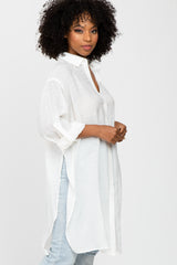 woman wearing a long white button-up shirt with a relaxed fit and side slits, paired with light blue jeans