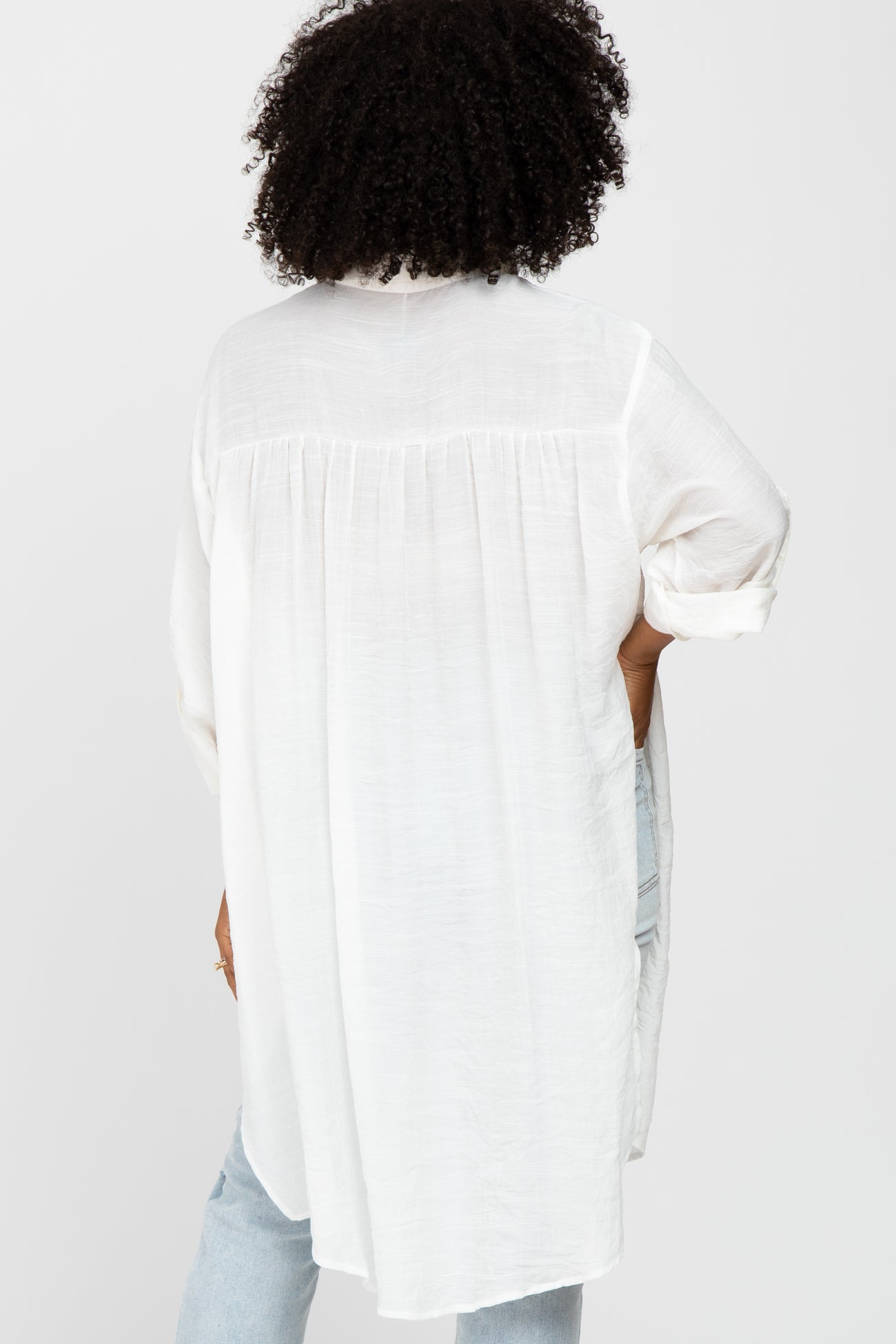 woman wearing a white long sleeve top with a flowy back design and rolled-up sleeves