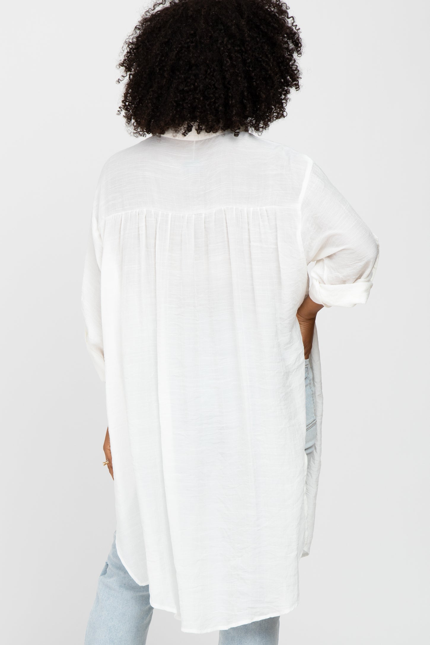 woman wearing a white long sleeve top with a flowy back design and rolled-up sleeves