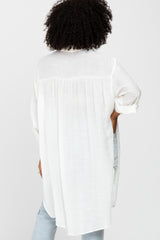 woman wearing a white long sleeve top with a flowy back design and rolled-up sleeves