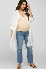woman wearing a long white button-up shirt over a beige maternity tank top and distressed jeans, showing a baby bump