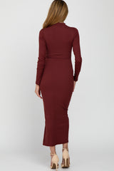 woman wearing a burgundy long sleeve fitted maternity dress with a side slit