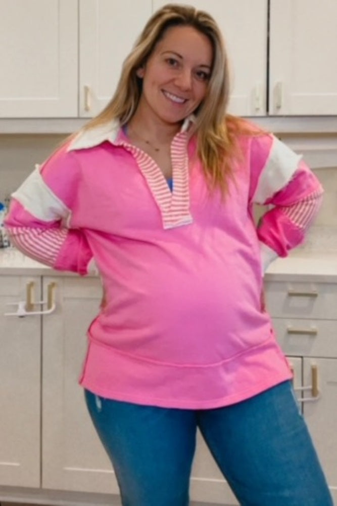 woman wearing a pink maternity pullover with striped sleeves and a visible baby bump, posing in a kitchen