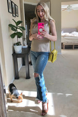 Woman in tan top and distressed jeans taking mirror selfie with pink phone and yellow crossbody bag