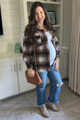 Smiling pregnant woman wearing a brown plaid shacket, white top, ripped jeans, and tan ankle boots.