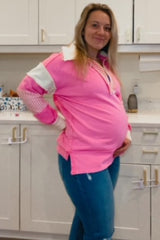 woman wearing a bright pink maternity pullover with a collar, holding her baby bump, paired with blue skinny jeans