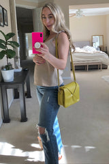 woman wearing a beige maternity tank top and distressed blue jeans, holding a yellow handbag and showing her baby bump