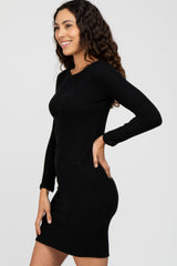 woman wearing a fitted black ribbed long sleeve dress, smiling and standing sideways