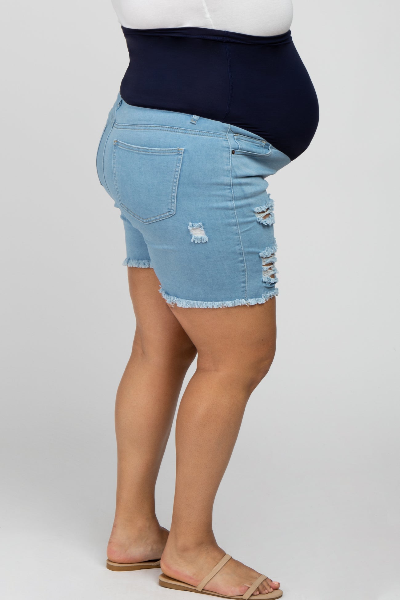 Side view of person wearing light wash distressed maternity denim shorts with a navy blue belly band