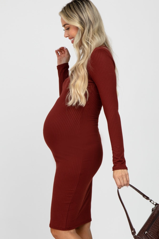 woman wearing a burgundy ribbed long sleeve maternity dress showcasing her baby bump and holding a handbag