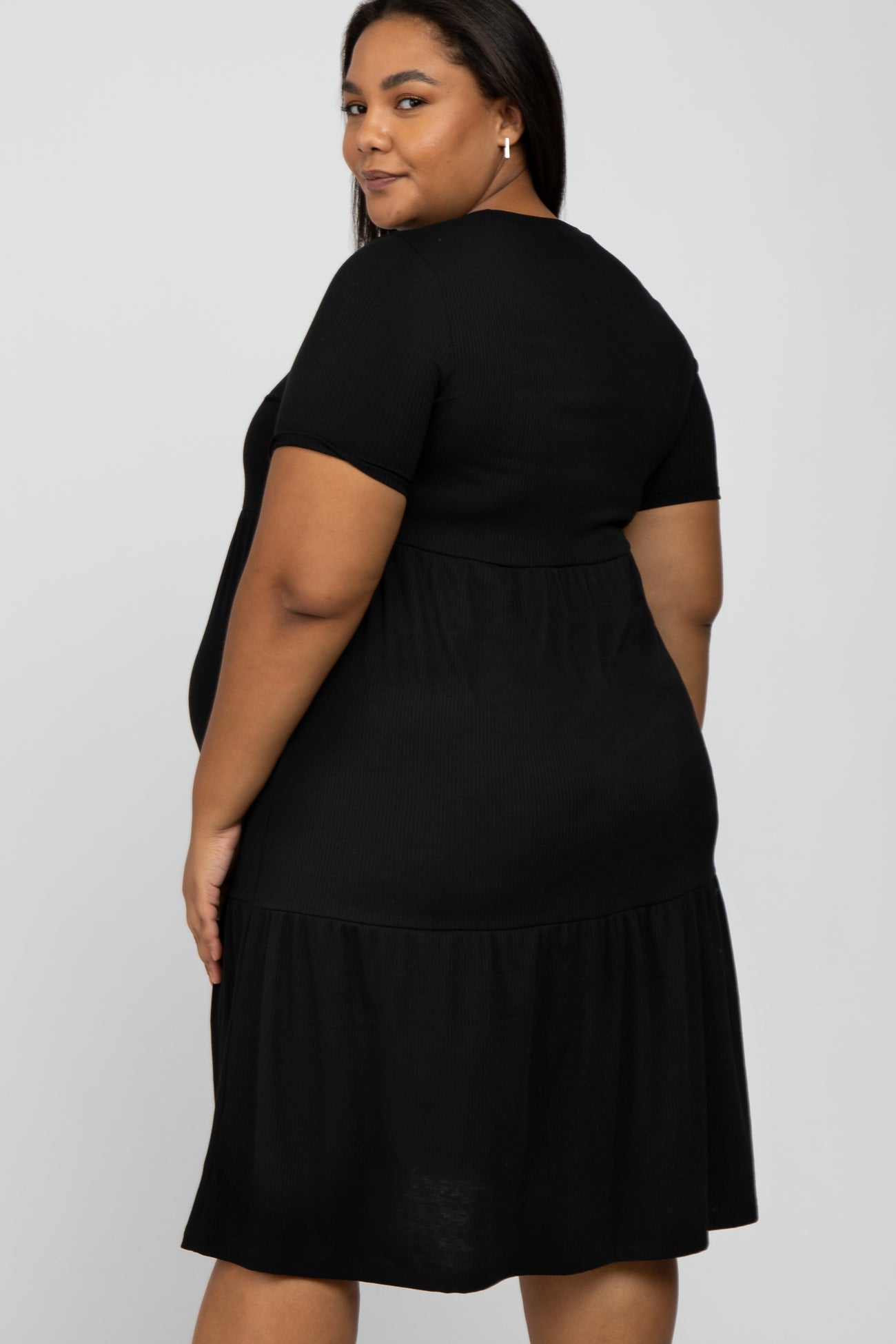 Woman wearing a short sleeve black tiered maternity dress against a white background