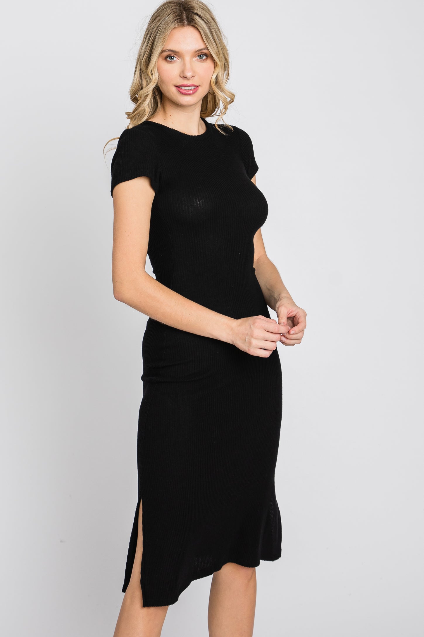 woman wearing a short sleeve black ribbed midi dress with a side slit against a white background