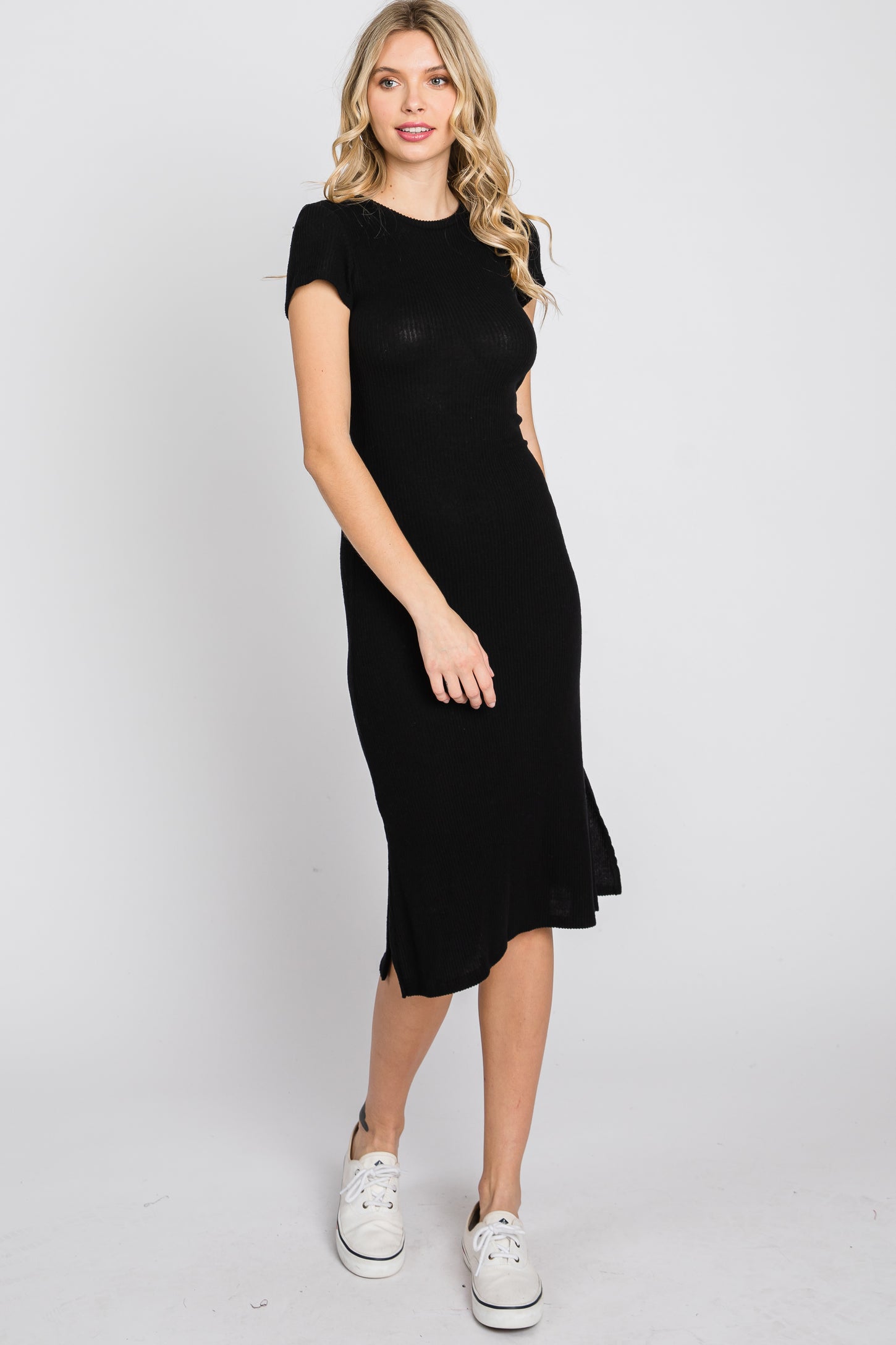 woman wearing a short sleeve black ribbed midi dress and white sneakers against a white background