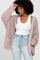Woman wearing a mauve oversized chunky knit cardigan over a white tank top and light wash jeans
