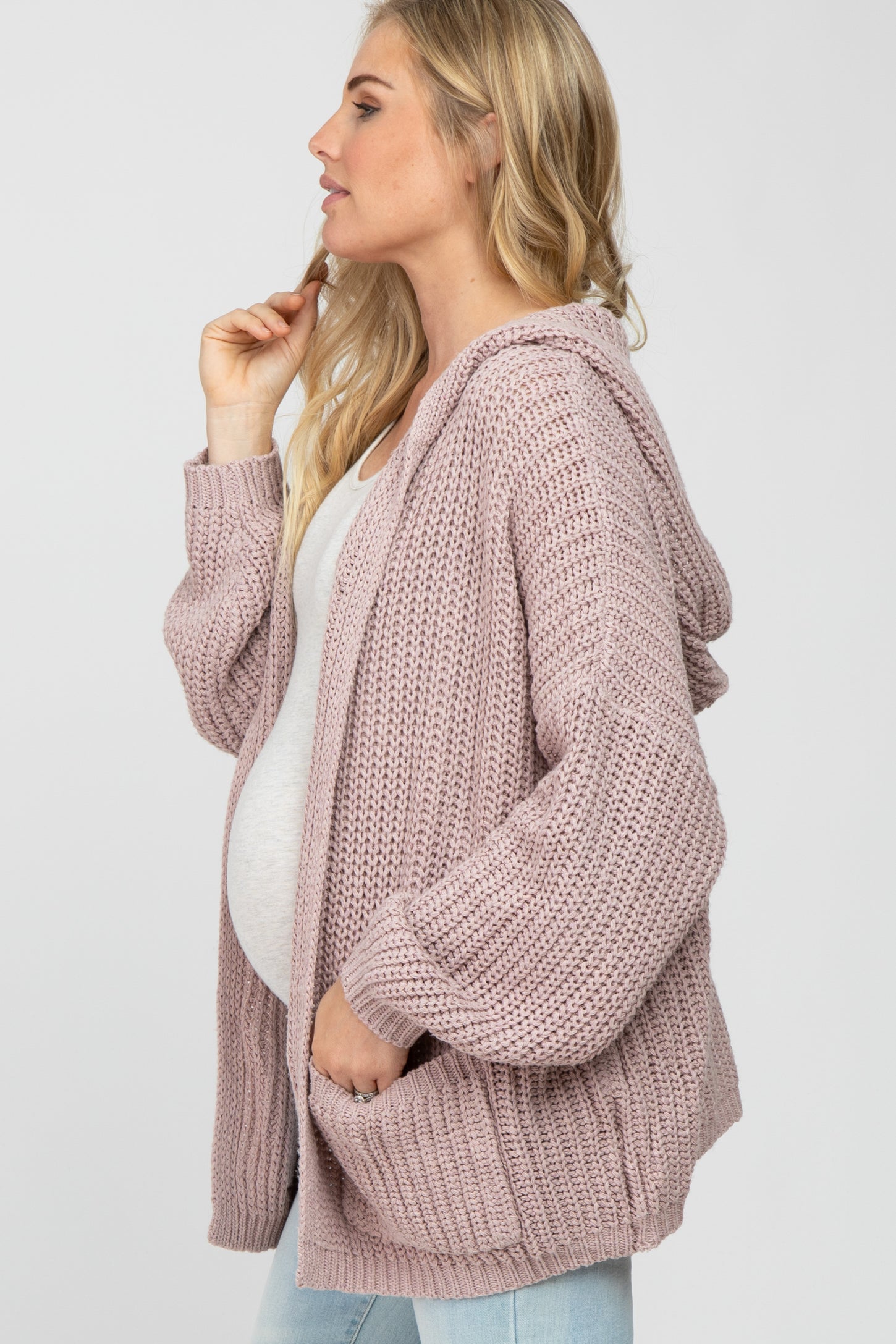 Pregnant woman wearing a mauve oversized knit hooded maternity cardigan over a white top and jeans