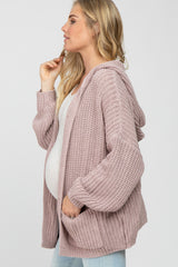 Pregnant woman wearing a mauve oversized knit hooded maternity cardigan over a white top and jeans
