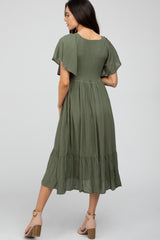 woman wearing a green maternity dress with short flutter sleeves and a tiered ruffle hem, showing a baby bump