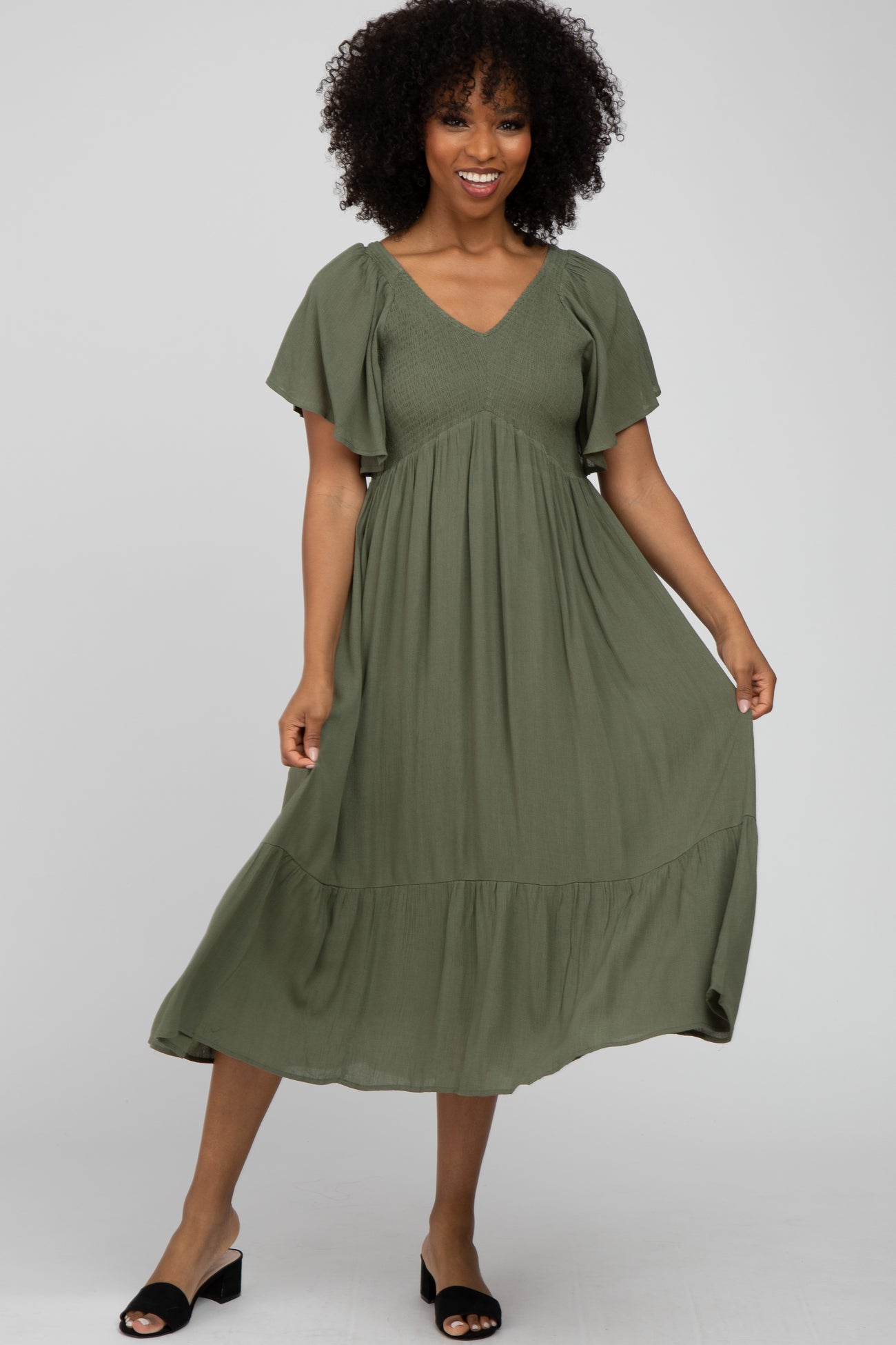 woman wearing a short sleeve olive green midi dress with a v-neck and tiered hem, smiling at the camera
