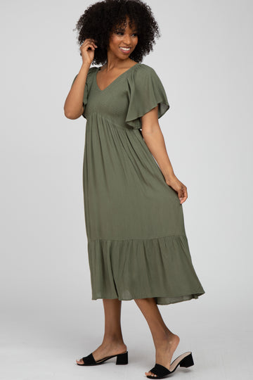 woman wearing an olive green midi dress with flutter sleeves and a tiered hemline, standing sideways