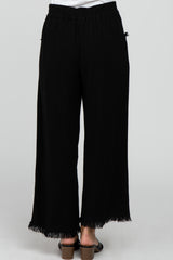 woman wearing black wide-leg pants with frayed hem and an elastic waistband, standing with her back to the camera