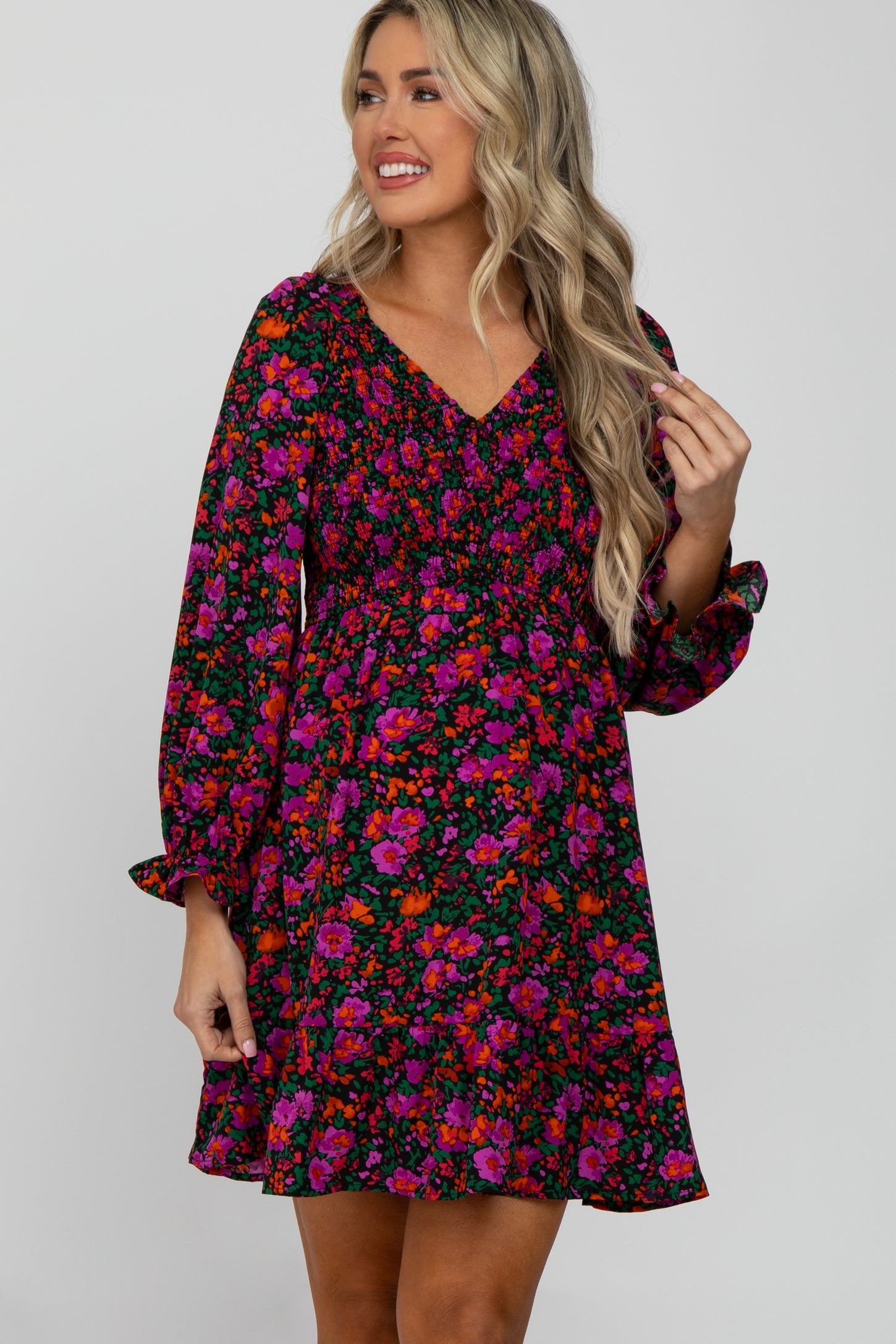 Woman wearing a long sleeve floral maternity dress with pink and orange flowers and smocked bodice