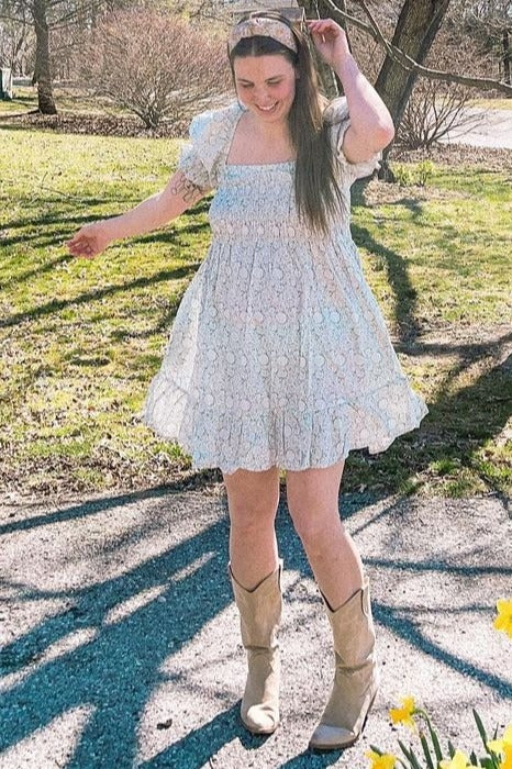 woman wearing a floral puff sleeve mini dress and tan cowboy boots standing in a sunny park