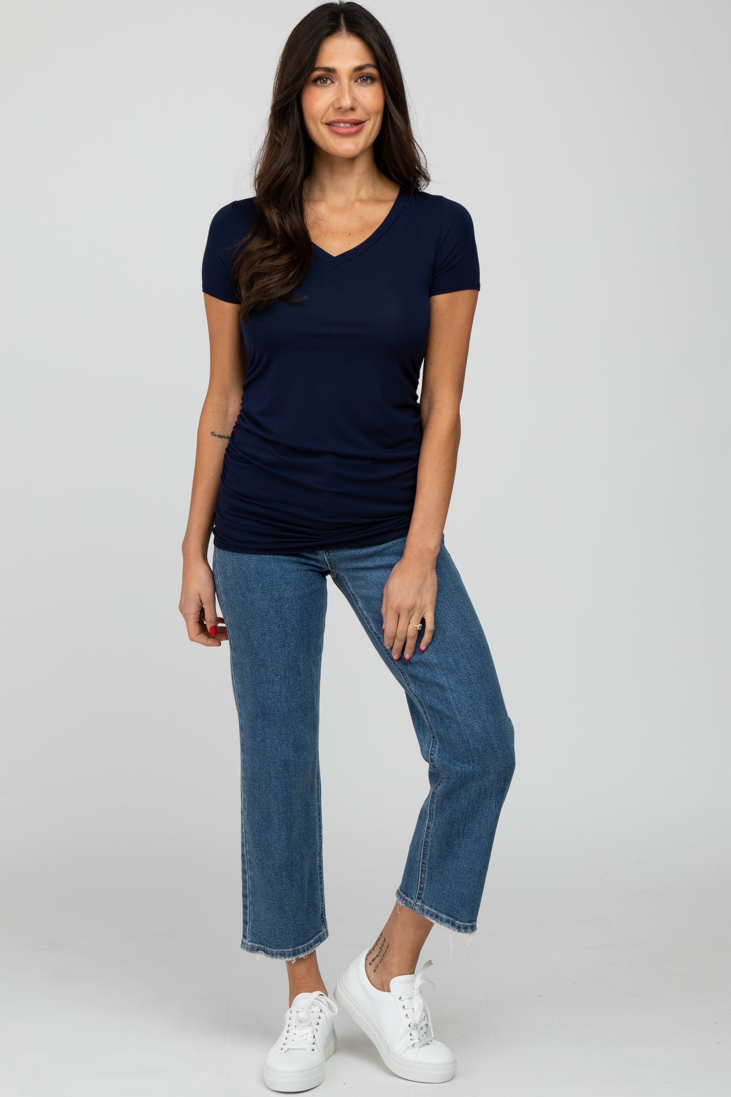 woman wearing a navy short sleeve v-neck top and light blue cropped jeans with white sneakers