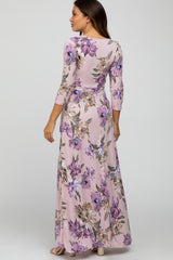 Woman wearing a light pink floral maternity maxi dress with purple flowers and three-quarter sleeves