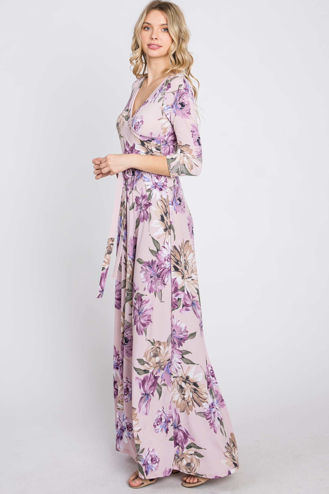 woman wearing a long sleeve floral maxi wrap dress in light pink with purple and tan flowers