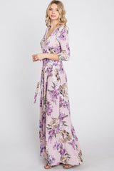 woman wearing a long sleeve floral maxi wrap dress in light pink with purple and tan flowers