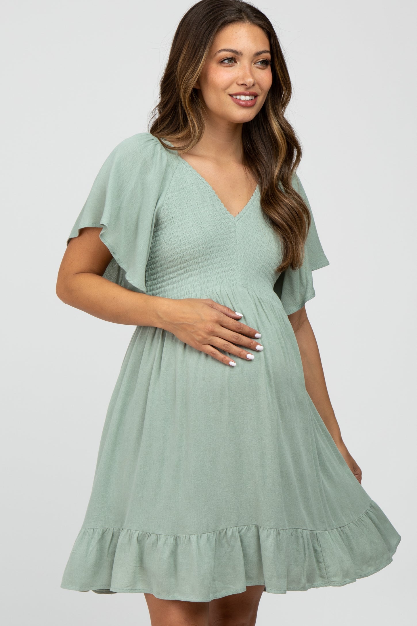 woman wearing a mint green maternity dress with flutter sleeves and a ruffled hem, holding her baby bump