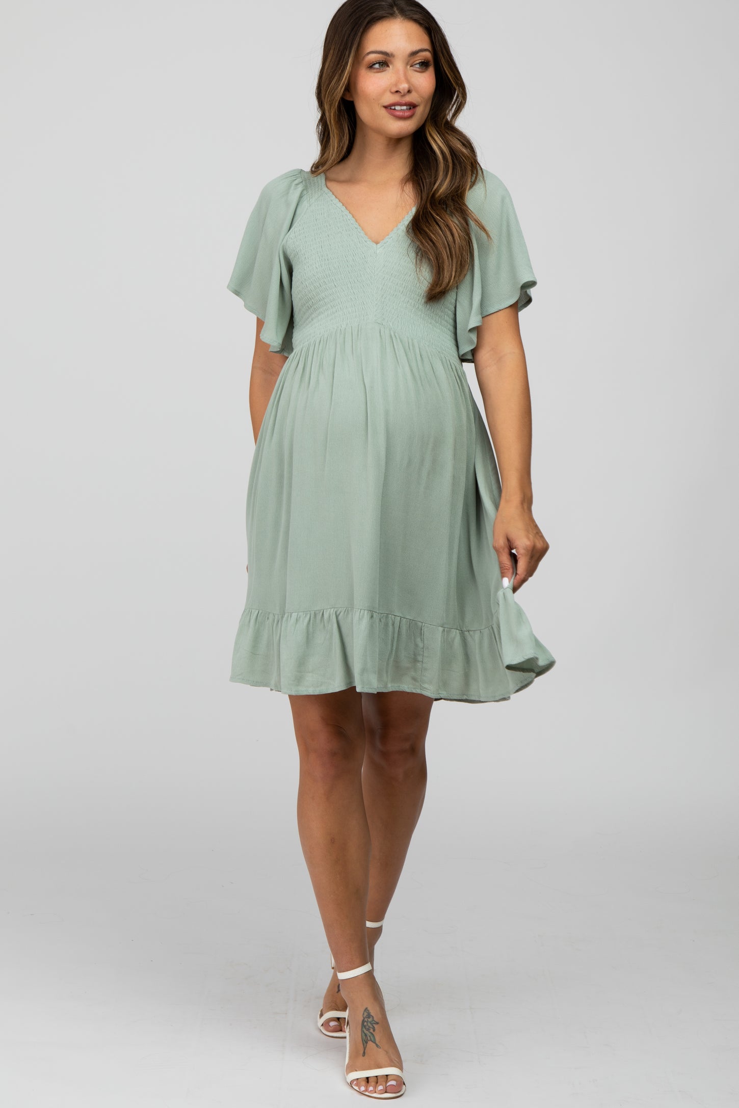 woman wearing a mint green maternity dress with flutter sleeves and a flowing skirt, showcasing her baby bump