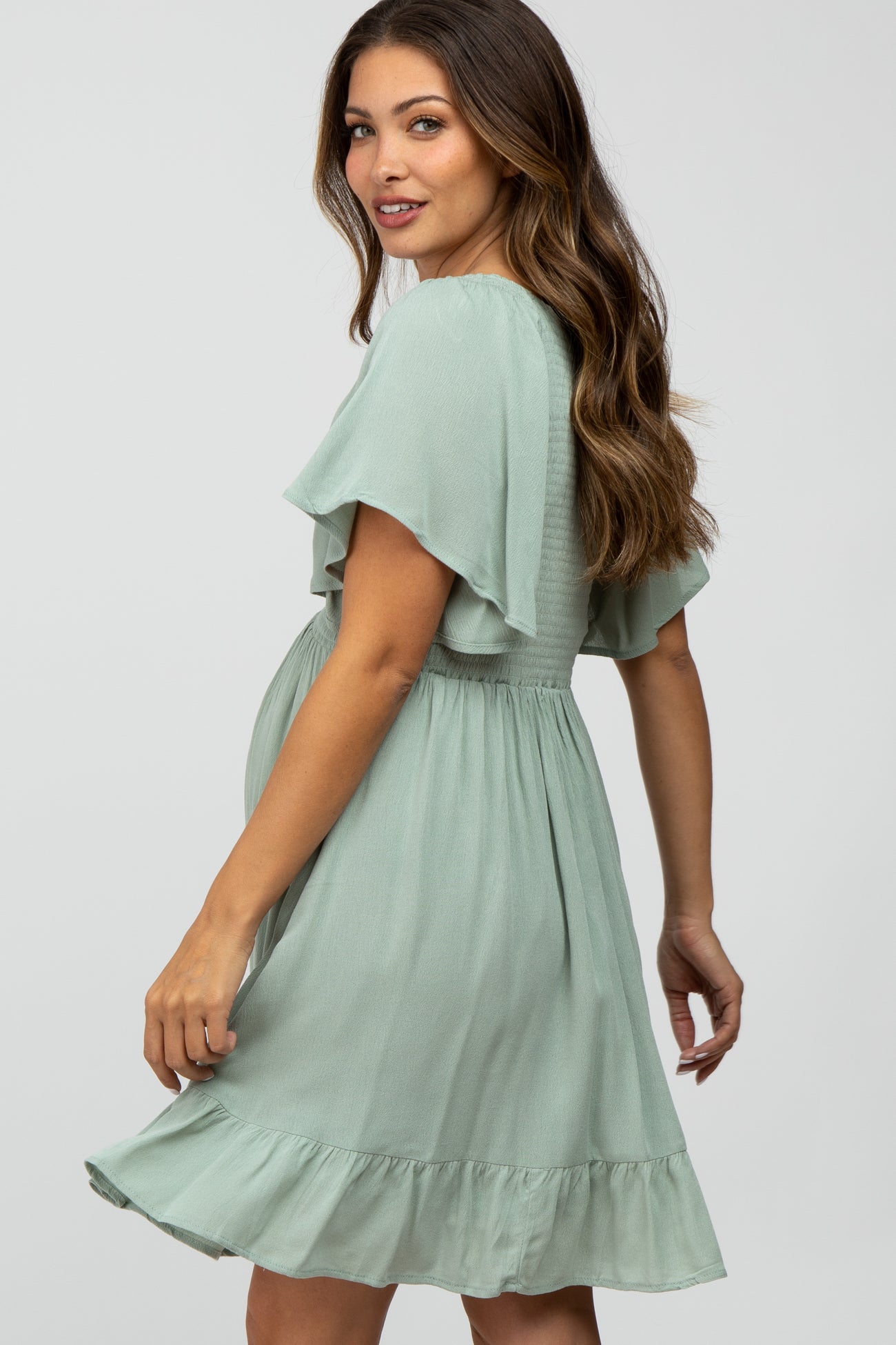 woman wearing a light green maternity dress with flutter sleeves and a ruffled hem, showing her baby bump